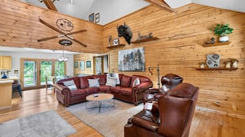 A spacious living room with a leather sofa, a brown leather armchair, and a wooden ceiling with exposed beams.