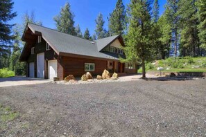 A log cabin with a gravel driveway and large boulders in front.