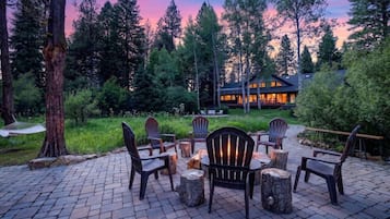 A patio with Adirondack chairs, a fire pit, and a stone firewood storage area.