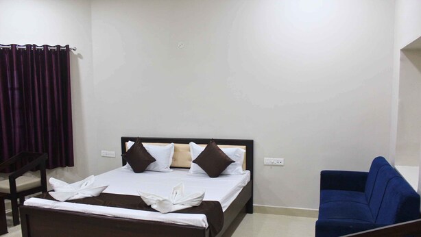 A bedroom with a bed, a blue sofa, a wooden chair, and a small rug. - Hotel Yubraj (Puri)