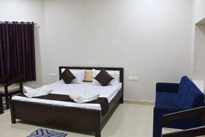 A bedroom with a bed, a blue sofa, a wooden chair, and a small rug.