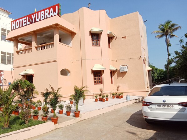 A hotel named "HOTEL YUBRAJ" with a modern architectural style, featuring a flat roof, multiple balconies, and a variety of potted plants in the foreground.