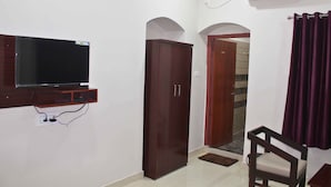 A room with a flat-screen TV mounted on the wall, a wardrobe, a door leading to another room, and a chair. - Hotel Yubraj (Puri)