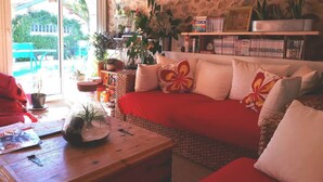 Un salon chaleureux avec un mur en pierre, un canapé rouge et une bibliothèque remplie de livres et d’objets décoratifs.