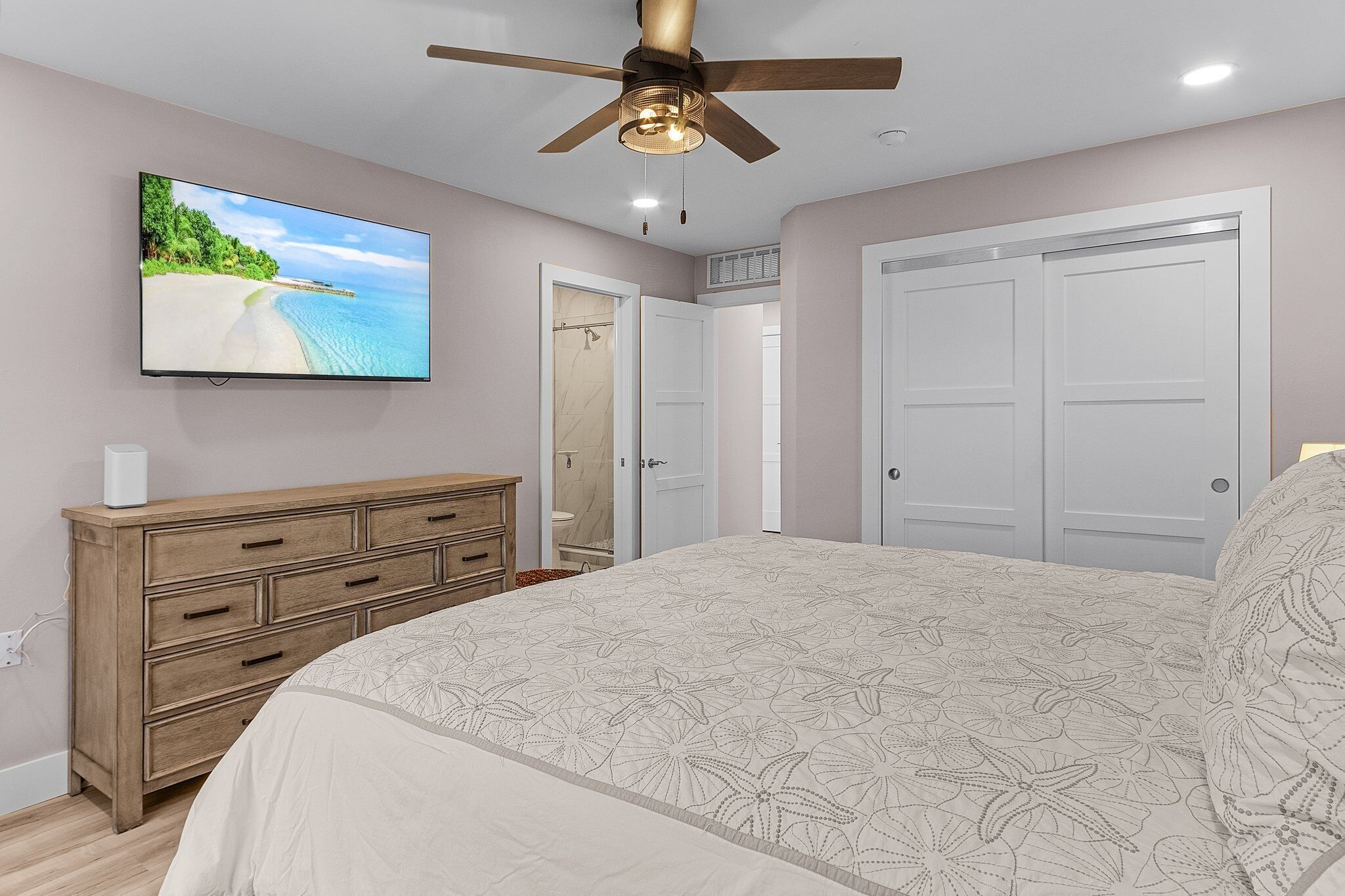 A bedroom with a bed, a dresser, a ceiling fan, a TV, and a closet.