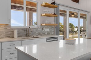 A modern kitchen with a large island, a built-in dishwasher, and a window overlooking a residential area.