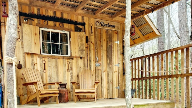 Une cabane en bois avec une véranda, deux fauteuils Adirondack et une pancarte sur laquelle on peut lire « Raelean ».