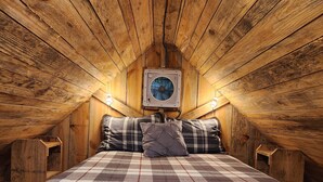 Une chambre confortable située sous les toits, avec une couvre-lit à carreaux, des murs en bois et un climatiseur fixé au mur.