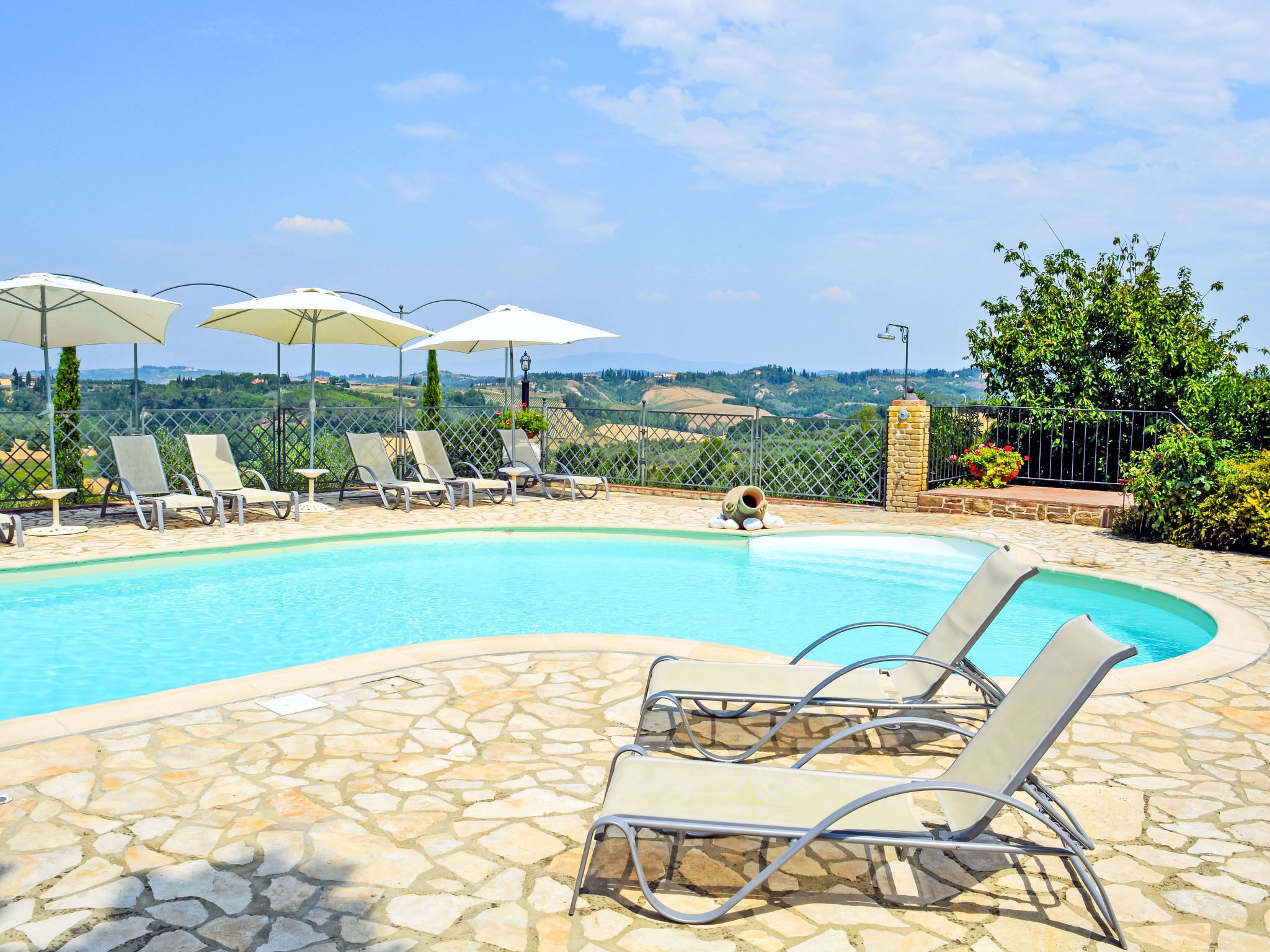 Zona de piscina con sillas de descanso y sombrillas, rodeada de suelo de piedra y una vista panorámica.