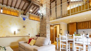 Amplia sala de estar con techo alto, un pilar de piedra, un sofá con cojines, una mesa de comedor con sillas y una zona de cocina con armarios de madera.