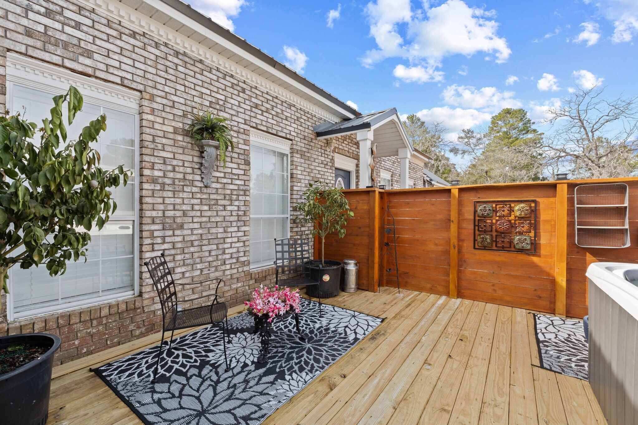 A wooden deck with a patio table and chairs, a potted plant, and a decorative wall panel.