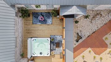 A rooftop patio with a hot tub, seating area, and potted plants.