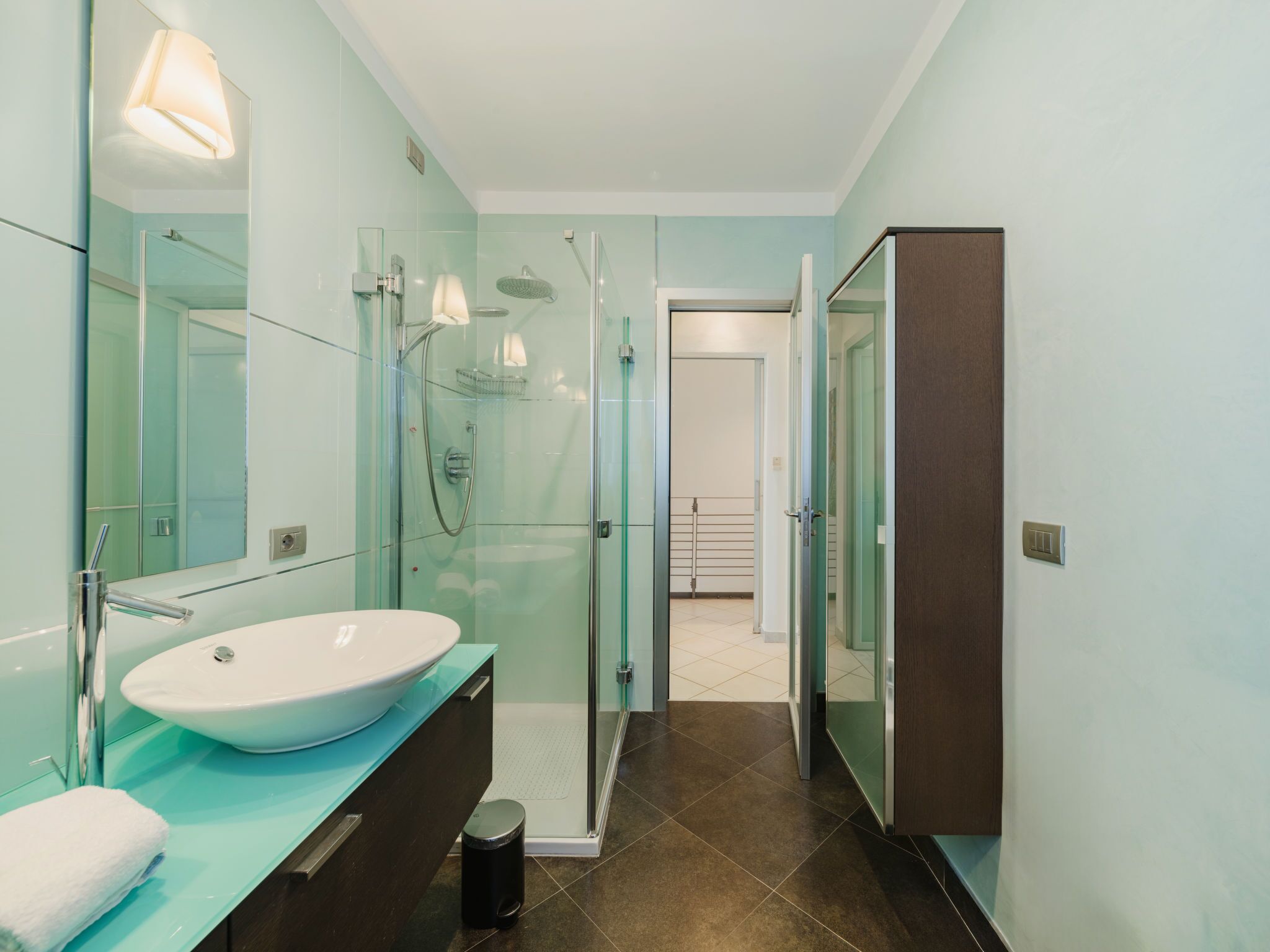 A modern bathroom with a large white sink, glass shower enclosure, and a dark wooden cabinet.