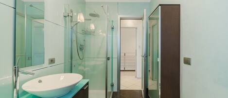 A modern bathroom with a large white sink, glass shower enclosure, and a dark wooden cabinet.