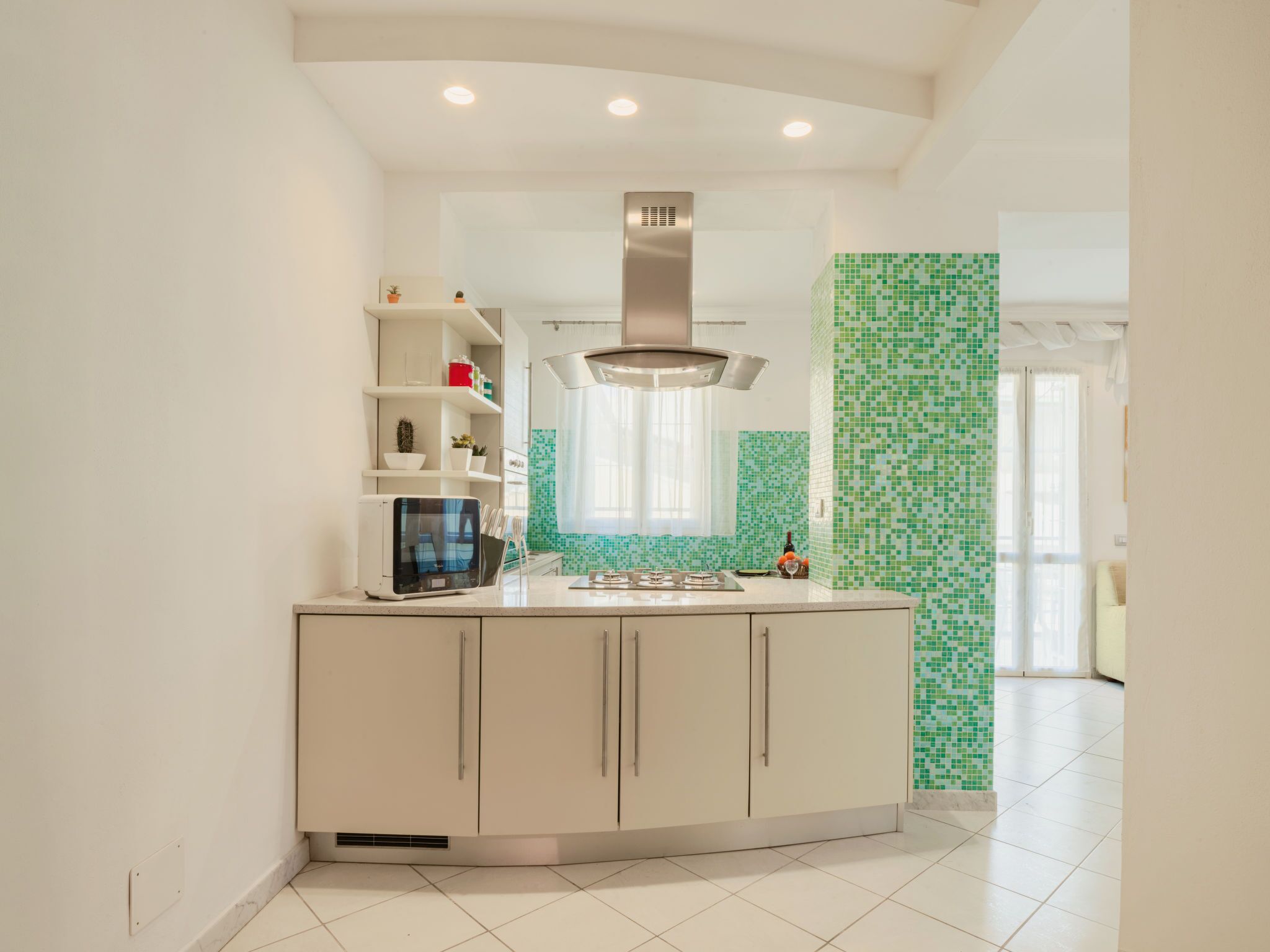 A modern kitchen with white cabinetry, a stainless steel range hood, and green mosaic tiles.