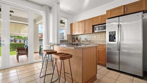 A modern kitchen with a stainless steel refrigerator, wooden cabinets, and a large island with stools. - Lakeside Escape | Stylish Unit with BBQ and Pool (Humacao)