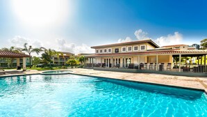 A swimming pool with a clear blue water surface, surrounded by a building with a tiled roof and multiple windows. - Lakeside Escape | Stylish Unit with BBQ and Pool (Humacao)