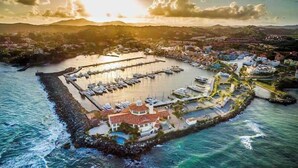 An aerial view of a coastal marina with multiple docks and boats, surrounded by a residential area with houses and a prominent building with a red roof. - Lakeside Escape | Stylish Unit with BBQ and Pool (Humacao)