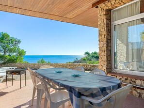 Un espace extérieur abrité, aménagé pour prendre les repas, avec une table et des chaises, offrant une vue panoramique sur la mer.