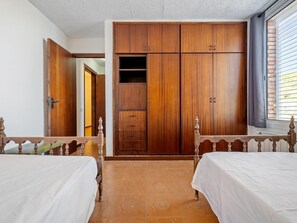 Une chambre avec deux lits, une armoire et une fenêtre avec des stores.