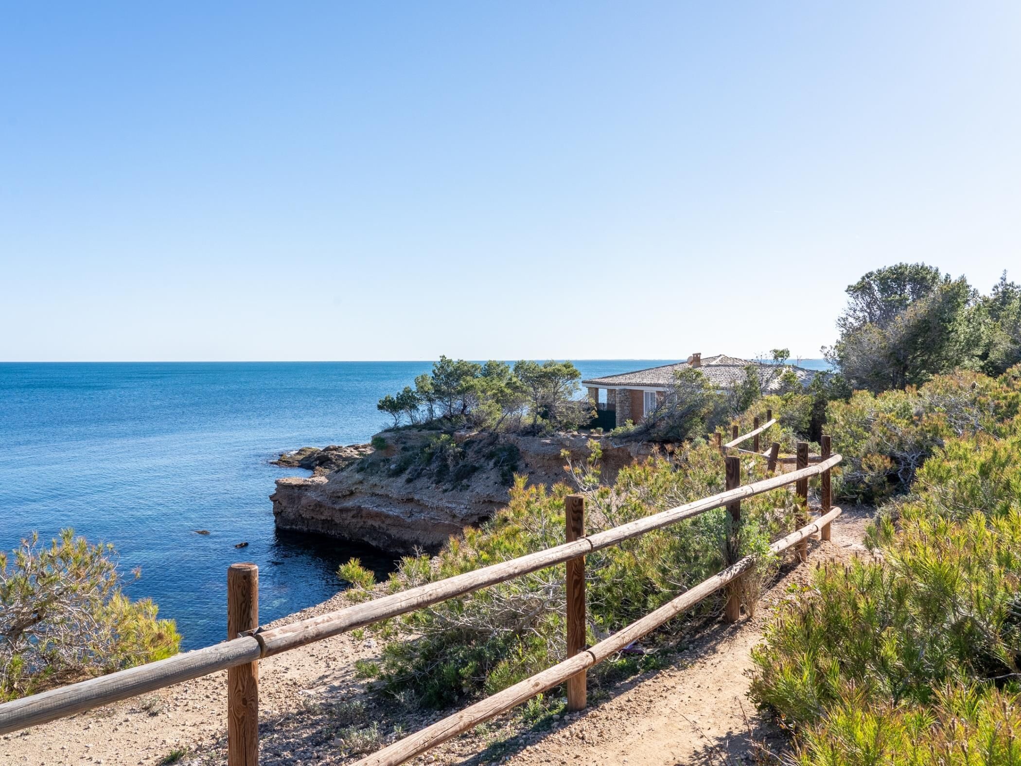 Una propiedad costera con valla de madera, un edificio de piedra y vista al mar.