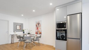 A modern kitchen with a stainless steel refrigerator, built-in oven, and microwave. There is a dining table with chairs and a vase of flowers.