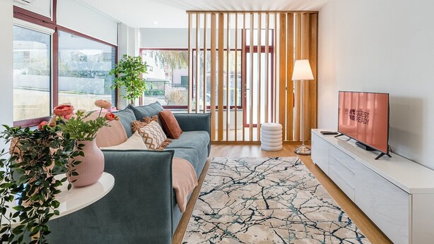 A modern living room with a sofa, a TV, a lamp, and a large window with a view of the outside.