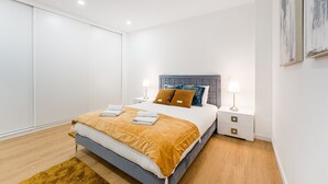 A modern bedroom with a large bed, two bedside tables, a headboard, and a floor-to-ceiling sliding door.