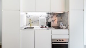 A modern kitchen with white cabinetry, a marble backsplash, a gold faucet, a coffee machine, and an oven. - GuestReady - Restful haven in Porto (Porto)