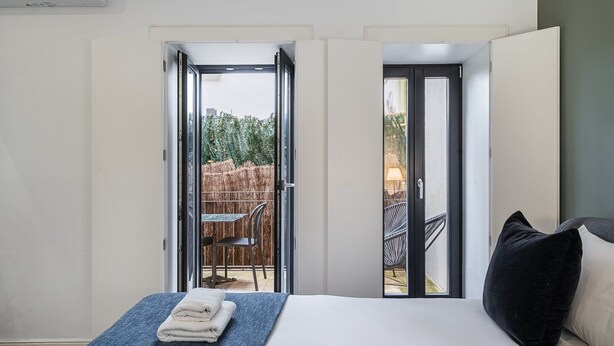 A bedroom with a bed, a blue blanket, and a view of an outdoor patio with chairs and a table. - GuestReady - Restful haven in Porto (Porto)