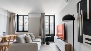 Una habitación de hotel moderna con sofá, mesa de comedor, televisor y ventanas grandes.