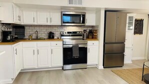 A modern kitchen with white cabinets, stainless steel appliances, and a wooden countertop. - Cozy Studio - Long Term 1 Month + Only (Saginaw)