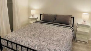 A bedroom with a bed, two bedside tables, a nightstand, a wardrobe, and a hanging light fixture. - Cozy Studio - Long Term 1 Month + Only (Saginaw)