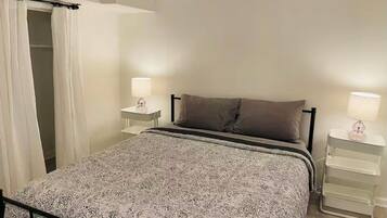 Une chambre à coucher comprenant un lit, deux tables de chevet, une commode, une armoire et un luminaire suspendu.