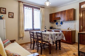 A kitchen with wooden cabinets, a dining table with chairs, a refrigerator, and a window with curtains.