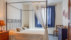 Una cama con dosel y cuatro columnas, un aparador de madera, una silla y un escritorio con lámpara.