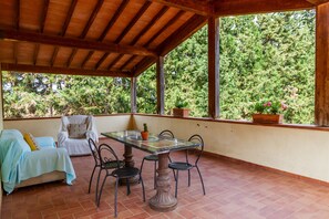 An outdoor patio with a table and chairs, a covered seating area, and a view of a forested area. - Apartment 'Calasole' with Shared Pool, Wi-Fi and Air Conditioning (Grosseto)