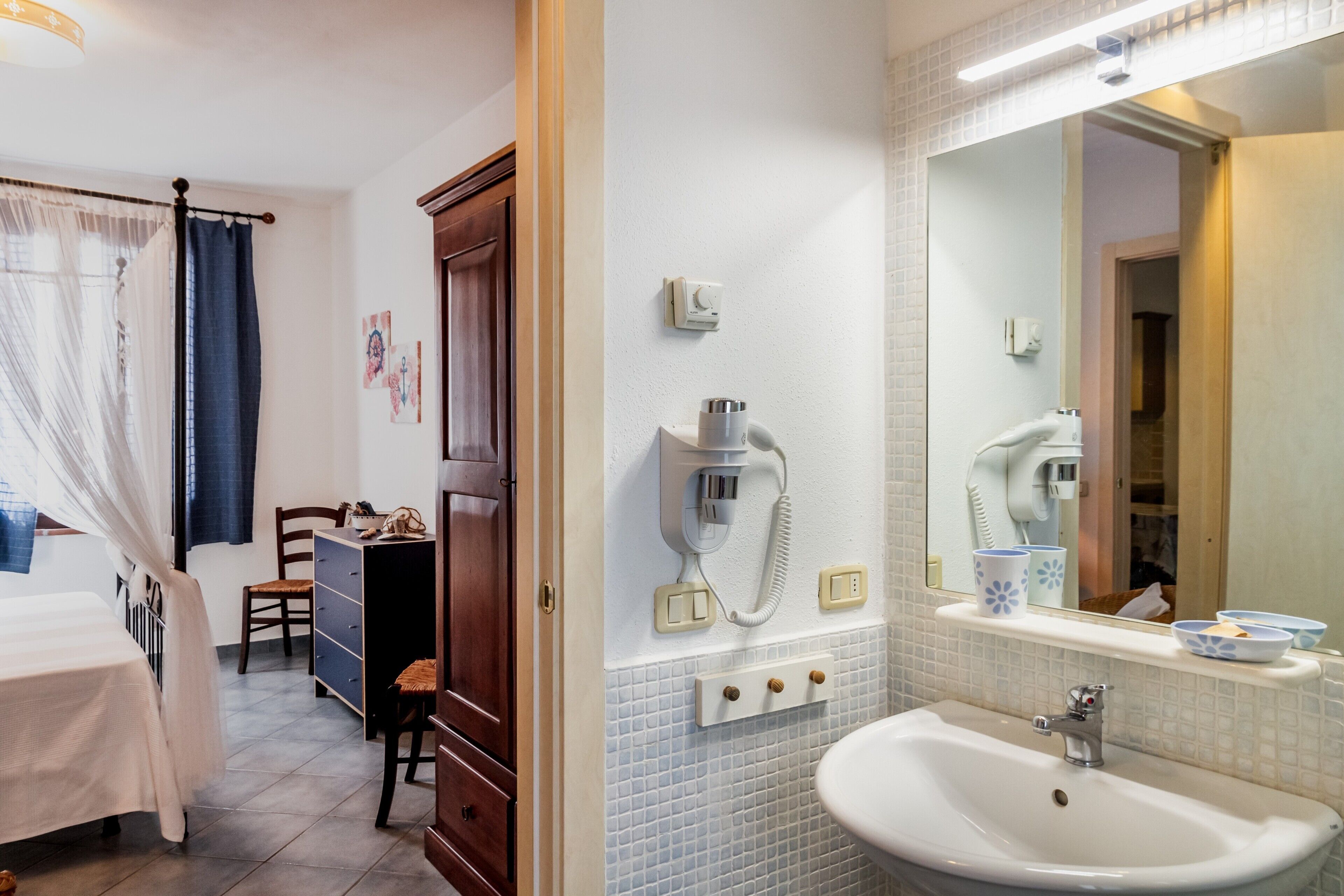 A hotel room with a bed, a chair, a dresser, a bathroom with a sink, a mirror, and a telephone.