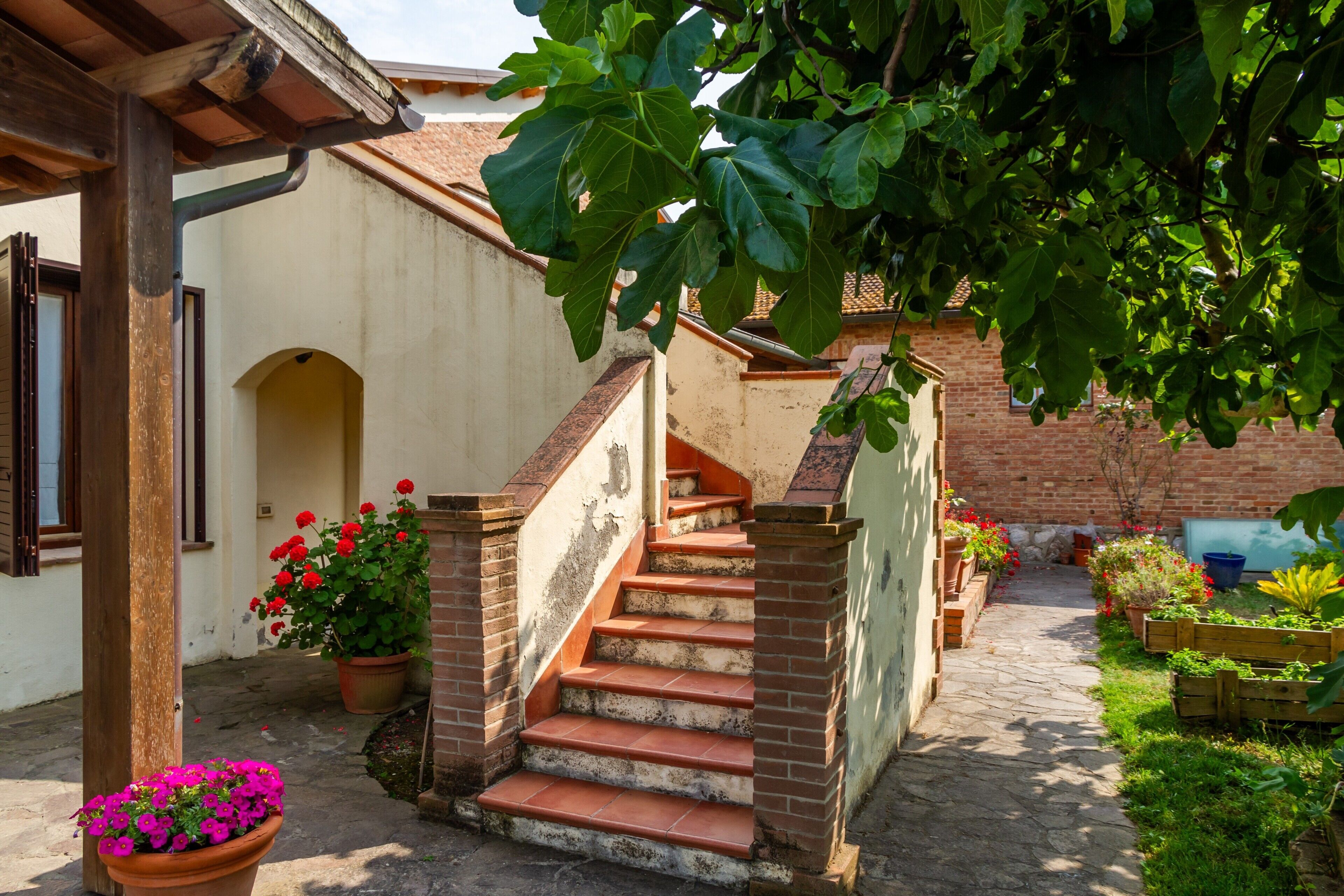 A staircase leading to a building with a brick exterior and a garden area with potted plants and flowers.