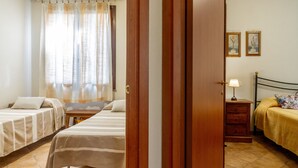 A hotel room with two beds, a wooden door, a nightstand with a lamp, and two framed pictures on the wall. - Apartment 'Amelia' with Shared Pool, Wi-Fi and Air Conditioning (Grosseto)