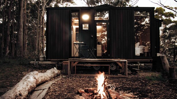 Eine Holzhütte mit Kamin, einer Terrasse und einem sichtbaren Innenraum mit Stuhl und Tisch.