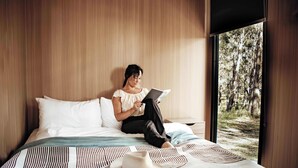 Eine Person sitzt auf einem Bett mit einem Laptop, einem Hut und einer gemusterten Decke.