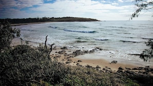 Eine Küstenlandschaft mit Strand, Wellen und einer entfernten Hügelkette.