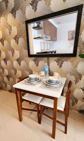 Un coin repas avec une table dressée pour deux personnes, une bouteille d’eau et un miroir au-dessus de la table qui reflète la pièce.