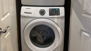 A front view of a laundry room with two stacked washers and dryers, a control panel, and a door. - Cozy 2-bedroom retreat – comfort, style, and relaxation await you (Bedford)