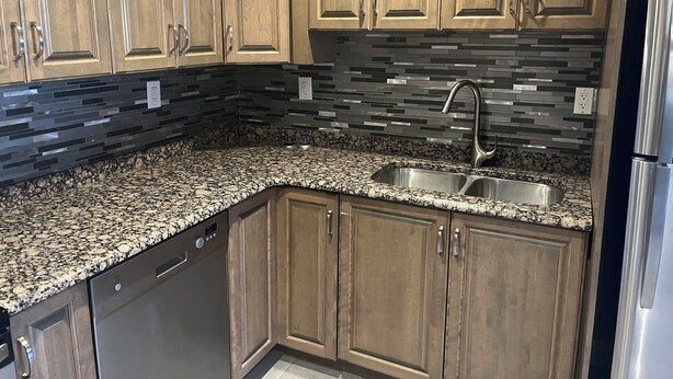 A kitchen with wooden cabinets, a granite countertop, a stainless steel sink, and a dishwasher. - Cozy 2-bedroom retreat – comfort, style, and relaxation await you (Bedford)
