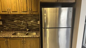 A kitchen with wooden cabinets, a stainless steel refrigerator, and a granite countertop with a sink. - Cozy 2-bedroom retreat – comfort, style, and relaxation await you (Bedford)