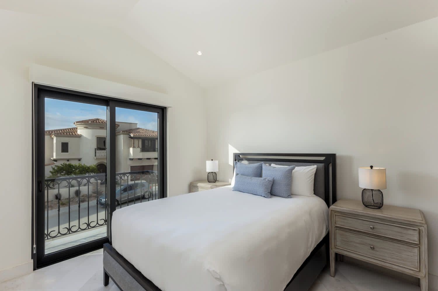 A bedroom with a large bed, a nightstand, a lamp, and a view of the outside through a sliding door.