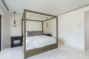 A four-poster bed with a white mattress and patterned pillows, a dark wooden nightstand, and two hanging pendant lights.