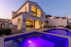A two-story house with a swimming pool, outdoor seating, and a well-lit patio area.